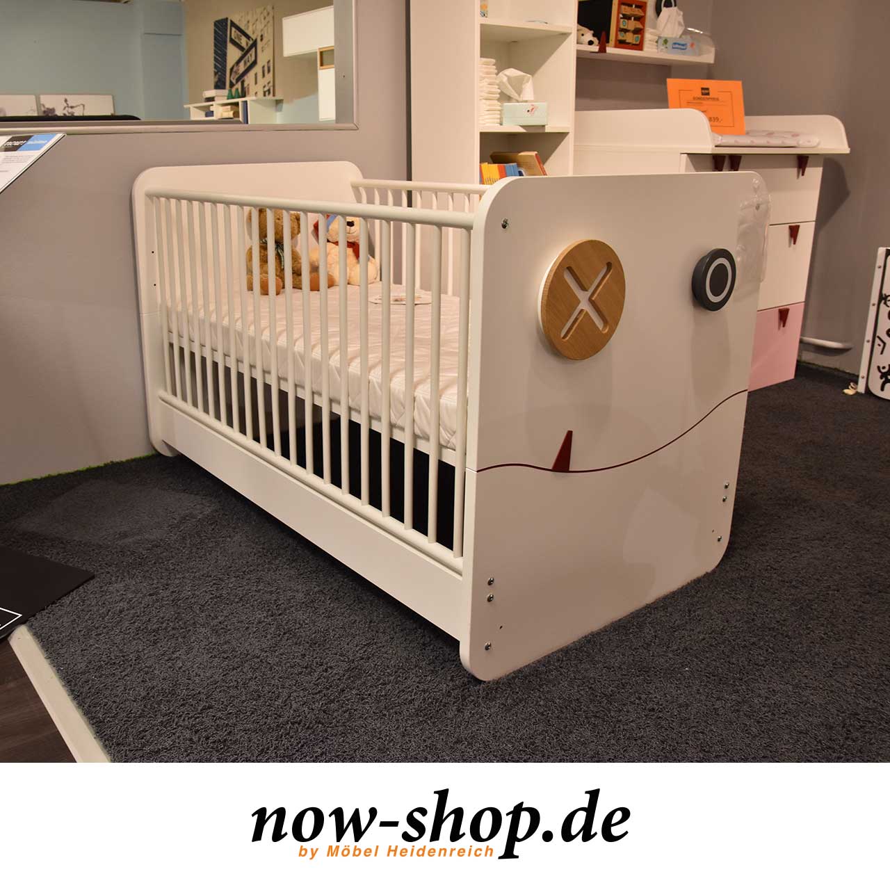 now! by hülsta - minimo Babybett mit Zubehör Ausstellungsstück Weißes Babybett mit Sprossen an der Seite. An der Front zwei Haken, die wir Augen aussehen und ein angedeuteter Mund mit rotem Zähnchen.
