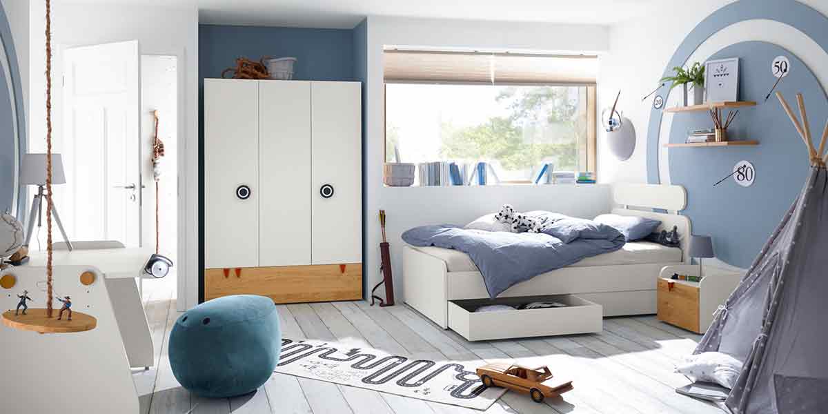 Titelbild Kinderzimmer Milieubild eines Kinderzimmers mit weißem Kinderbett und dreitürigem Schrank mit Holz-Akzent.