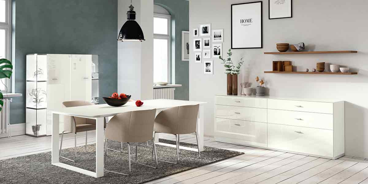 Titelbild Esszimmer Milieubild eines Esszimmers. Links eine Vitrine, in der Mitte ein weißer Tisch mit Schalenstühlen und rechts ein Sideboard.